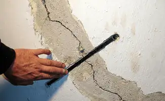 A wall with a large crack is being inspected by a professional in Shreveport, LA